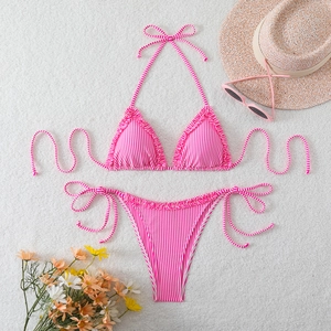 Flat lay of pink striped bikini set with ruffled edges, sun hat and sunglasses on fur