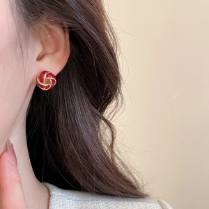 Close-up of spiral red enamel stud earring with gold border worn on ear lobe