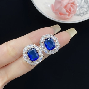 Close-up of silver stud earrings featuring blue square stones and white zircon accents