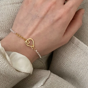 Macro detail of S925 sterling silver heart clasp on a two-tone chain bracelet