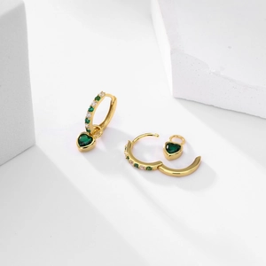 Detail of gold heart earrings with green heart stones and pavé accents on white props