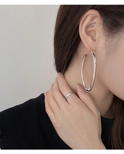 Close-up of model wearing large polished silver hoop earrings and a minimalist ring