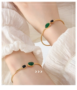 Close-up of gold plated open bangle with black and emerald green stones on model