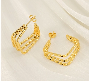 Detail of gold layered square hoop earrings with twisted rope texture on white silk fabric