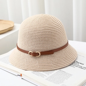 Detail of beige woven bucket hat featuring a brown leather strap and gold metal buckle