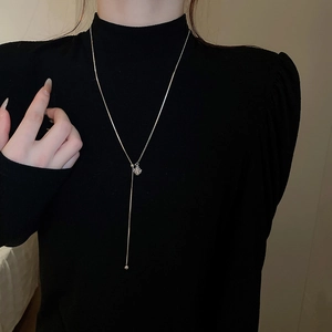 Detail of long Y-shaped necklace with gold square zircon and ball pendant on black outfit
