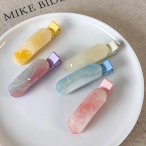 Detailed top view of 5 marble patterned duckbill hair clips in a white ceramic plate
