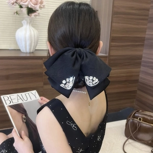 Close-up of a large black satin bow hair clip with luxury rhinestone details on a model