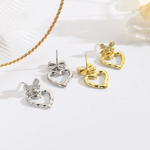 Orecchini a cuore e fiocco in oro e argento con strass lucidi su sfondo bianco pulito