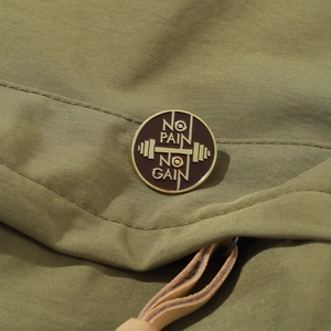 Macro detail of a round enamel gym badge with No Pain No Gain text on green fabric