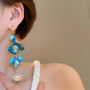Detail view of long gold tassel earrings with blue stones and seashell charms
