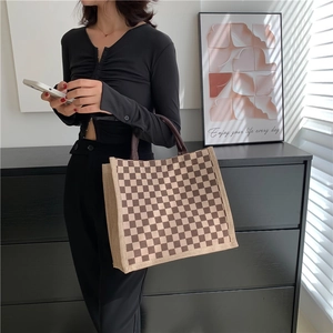 Checkerboard pattern burlap tote bag in brown and beige colors held by a model
