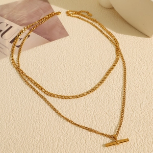 Collier double couche doré avec fermoir en T minimaliste sur fond texturé de qualité supérieure