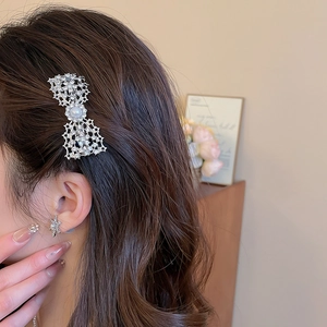 Detailed close-up of a silver bow hair clip with sparkling rhinestones and a large pearl