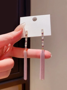 Detail of gold tassel earrings featuring purple cubic zirconia and hanging chain fringe