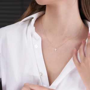 Close-up of a delicate 18K gold stainless steel cross necklace worn by a model in white