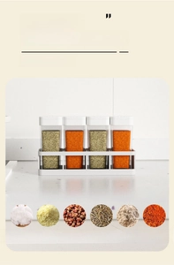 Detail of four transparent kitchen spice jars with white lids on a matching storage base