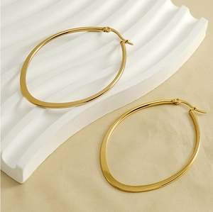 Macro detail of large gold oval hoop earrings on a textured minimalist background