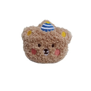Plush brown bear brooch with blue striped hat and curly texture on white background