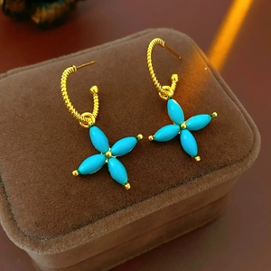 Macro view of gold-plated clover earrings with blue turquoise stones on brown velvet