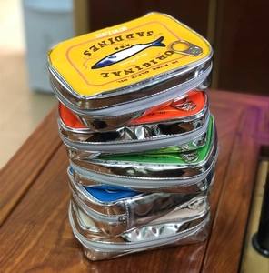 Close-up of sardine tin shaped cosmetic bags with zipper stacked on a wooden table