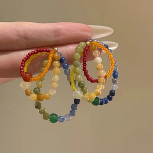 Close-up of handmade rainbow beaded earrings with gold hooks held against beige background
