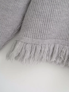 Close-up of grey knitted cardigan texture featuring soft chunky knit and fringe trim detail