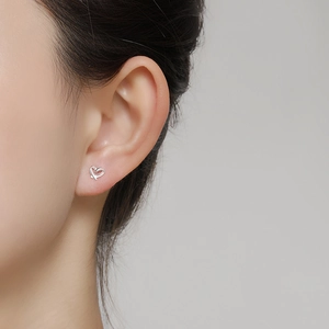 Close-up of minimalist S999 silver heart stud earrings worn by a model in soft lighting