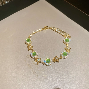 Close-up of gold bracelet featuring green stones, zircons and a small fish pendant