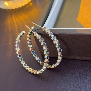 Detail showing colorful zircon gemstones set in gold C-shaped hoop earrings