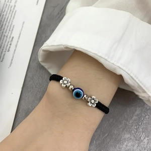 Detail of hand-woven black cord bracelet with blue evil eye bead and silver spacers