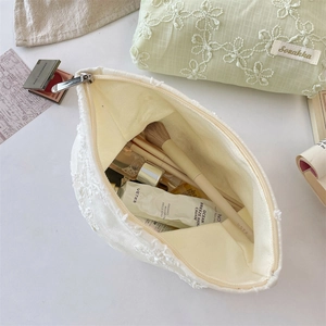 Macro shot of a white lace cosmetic bag showing detailed 3D floral embroidery and storage