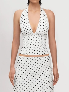 Detail of white polka dot halter top featuring deep V-neck and pleated chest design