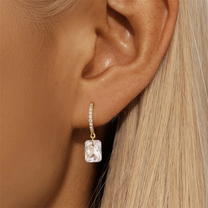 Detailed close-up of a model wearing a gold earring with a rectangle clear zircon stone