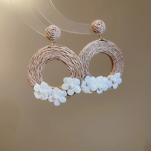 Detail of rattan earrings with white fabric flowers and pearls on a transparent stand