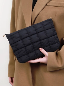 Fashionable black quilted makeup bag clutch held by a model in an elegant tan wool coat.