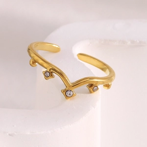 Macro detail of wave-shaped 18K gold-plated ring with four sparkling diamonds on white stone