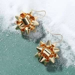 Close-up of golden festive ribbon ball drop earrings on a textured forest green base