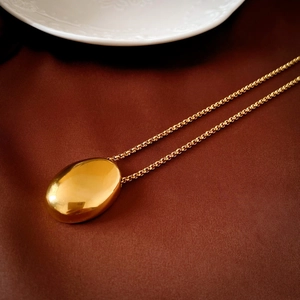 Detailed close-up of a smooth gold oval bean pendant on a fine necklace chain