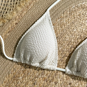 Macro detail of white seersucker bikini top on straw background for summer swimwear