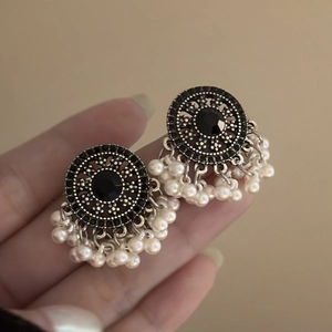Dettaglio di orecchini vintage con gemma nera e nappe di perle bianche in stile etnico