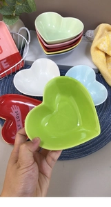 Detail showing hand holding a green heart-shaped ceramic bowl with various colors set