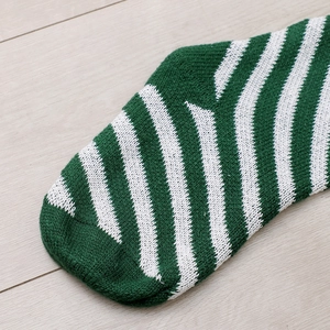 Detail of green and white striped knit stocking showing texture on a light wood floor