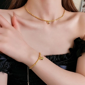 Golden heart necklace and bracelet set with fine beaded chain worn by a model