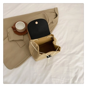 Detail of straw bucket bag featuring black leather flap and gold magnetic closure