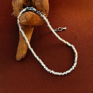 Detail of minimalist silver beaded bracelet with lobster clasp on a natural wood stand