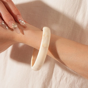 Detailed close-up of cream resin bangle with marble pattern on a linen background