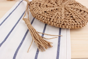 Close-up of circular woven paper straw bag featuring intricate tassels and natural texture
