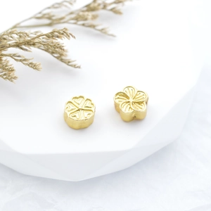 Matte gold flower spacers with heart and petal patterns on white geometric stand