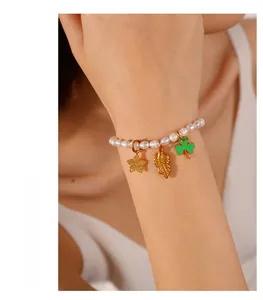 Detail of freshwater pearl bracelet with gold star leaf and green clover charms on wrist
